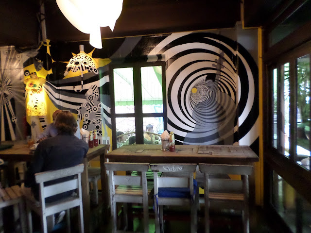 Intérieur du Blu Jazz Café avec fresques noir et blanc de spirales et de motifs graphiques sur les murs.
