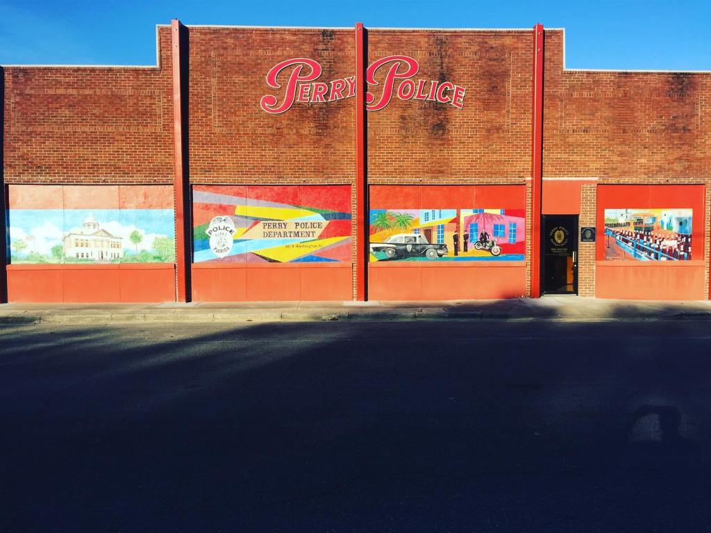 Fresque sur la façade du Perry Police Department avec le lettrage rouge « Perry Police » sur un mur de briques.
