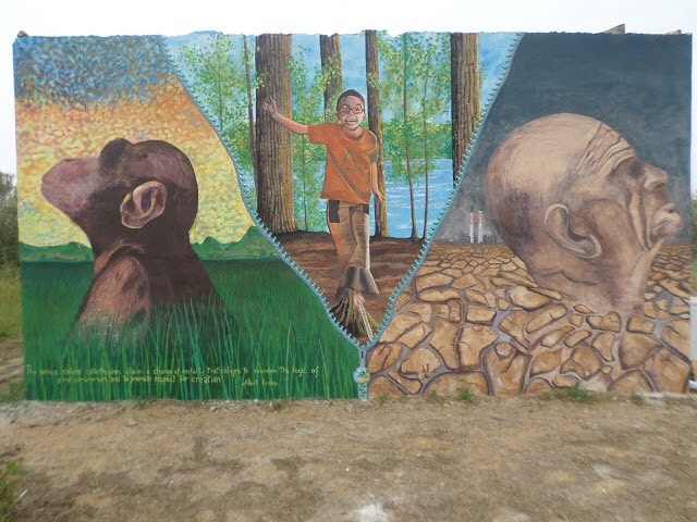 Fresque de la réserve de Biviere di Gela montrant deux figures simiesques et un enfant dans un paysage boisé.
