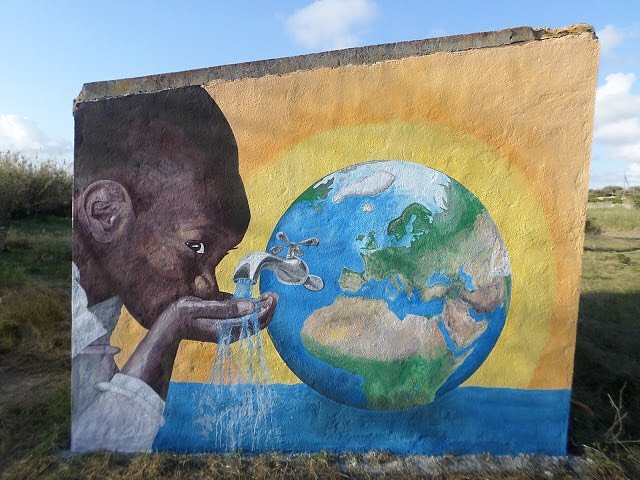Fresque de la réserve de Biviere di Gela représentant un enfant buvant à un robinet installé sur un globe terrestre.
