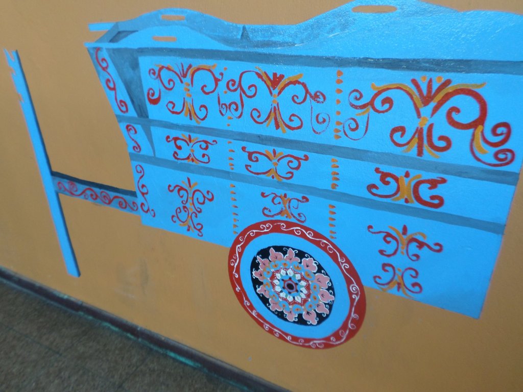 Panneau de charrette costaricaine bleu orné de motifs rouges et d’un médaillon floral peint.
