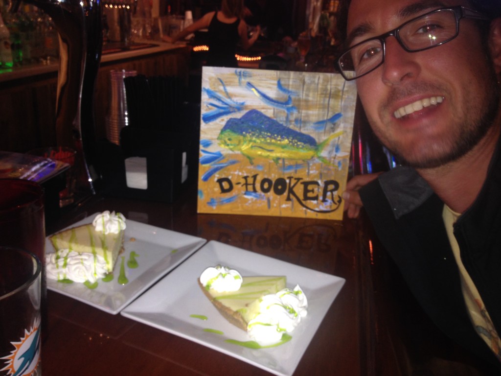 Petite peinture de paysage portant l’inscription « D-Hooker », posée sur une table de restaurant.
