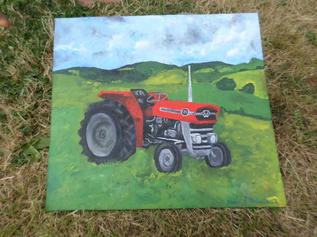 Peinture d’un tracteur rouge dans un paysage de collines vertes, posée dans l’herbe.
