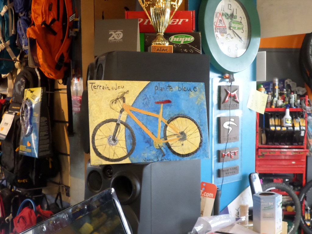 Peinture représentant un vélo jaune traversant une planète bleue, exposée dans un atelier de cycles.

