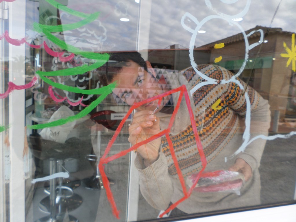 Sébastien Dubois peignant directement sur une vitrine avec des lignes rouges, vertes et blanches.
