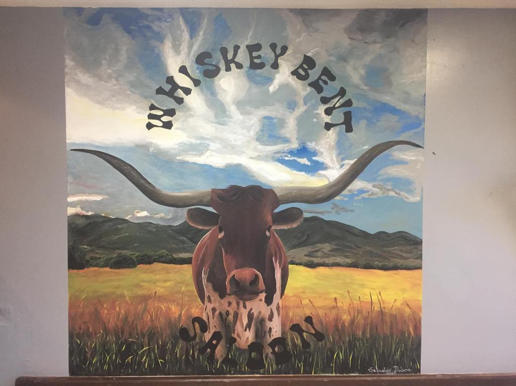 Fresque du Whiskey Bent Saloon représentant une tête de longhorn devant un paysage de prairie et de montagnes.
